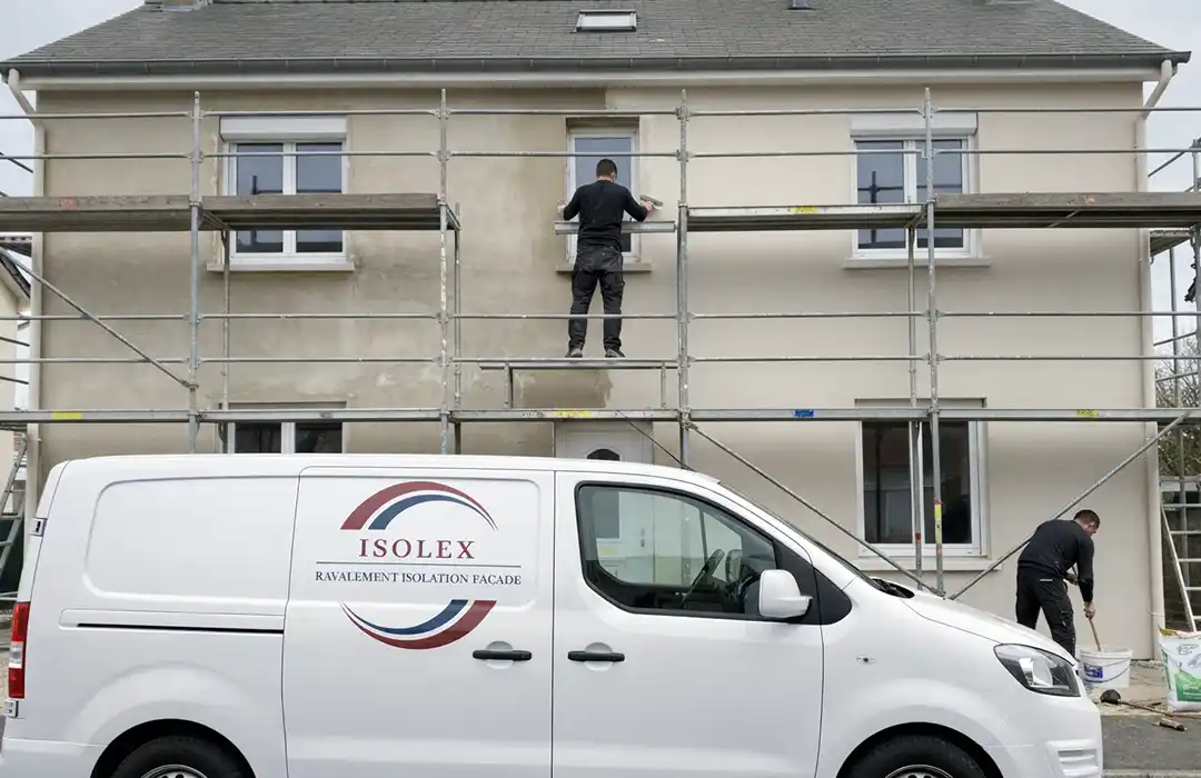 Isolex – Spécialiste ravalement, ITE et peinture extérieure Deux ouvriers rénovent l'extérieur d'une maison à l'aide d'un échafaudage. L'un se tient sur l'échafaudage, peignant près d'une fenêtre, tandis que l'autre travaille au niveau du sol à côté d'une camionnette de l'entreprise Isolex.