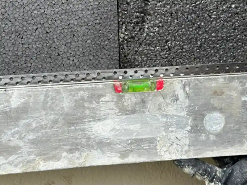 Traitement des ponts thermiques - Isolex Gros plan d'un niveau à bulle reposant sur une surface métallique devant des panneaux isolants en mousse noire, montrant que la surface est plane - une étape essentielle dans le traitement des ponts thermiques pour une efficacité énergétique optimale.